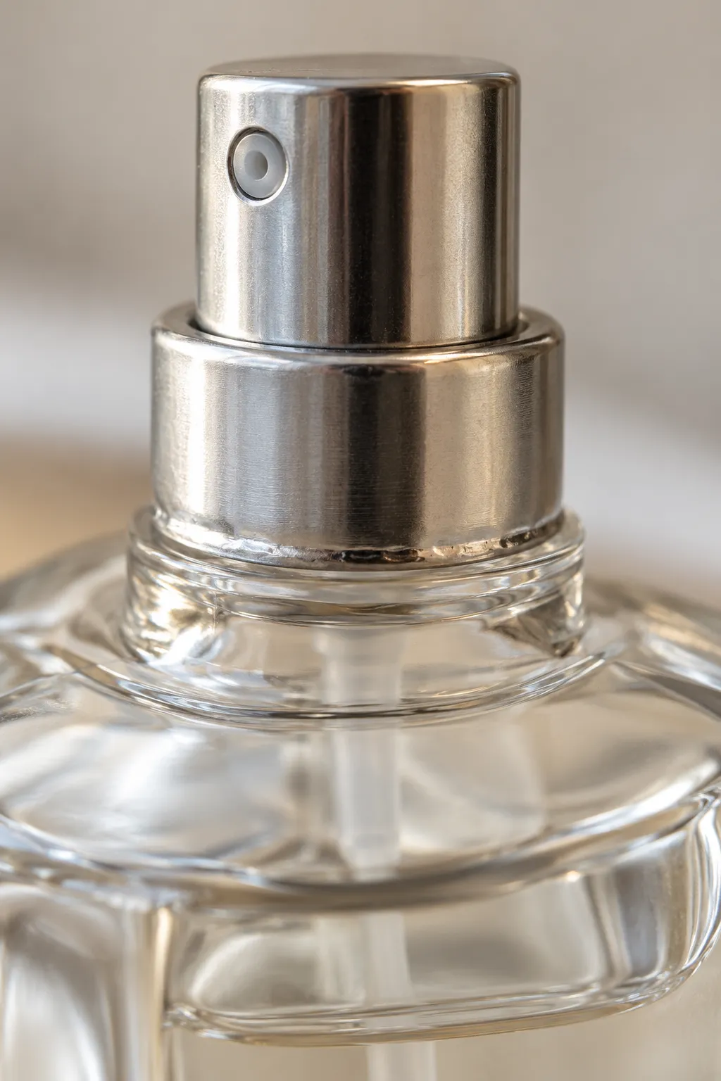 Macro view of a crimped aluminum collar and fine-mist pump pressed onto a perfume bottle neck, the mixed material assembly that decides whether perfume bottles can be recycled curbside